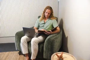 Male therapist Riley sitting on a brown leather couch at Nature Of Wellness in Currumbin, Gold Coast, providing online therapy.