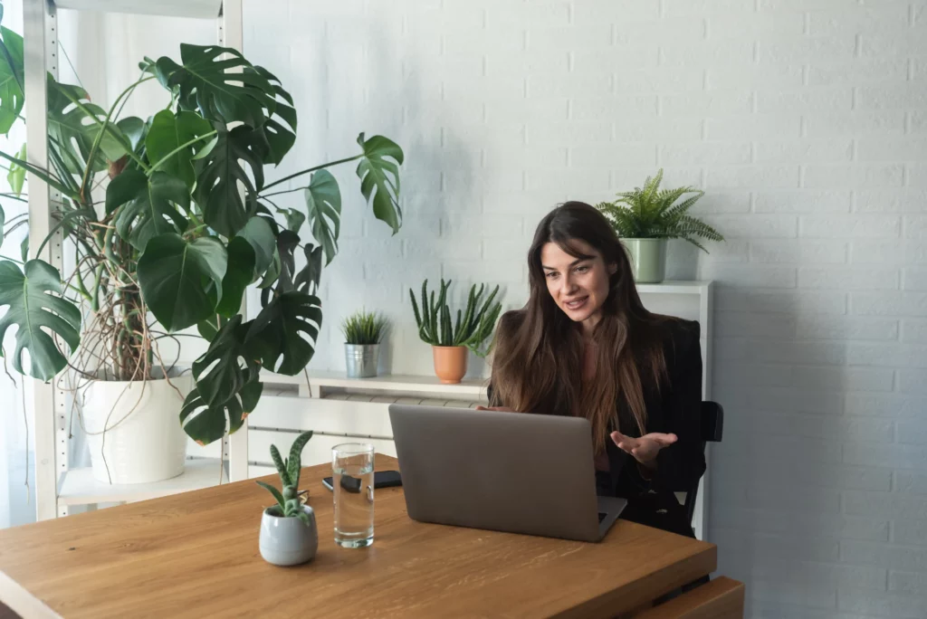 Woman smiling during online therapy session in home office surrounded by plants