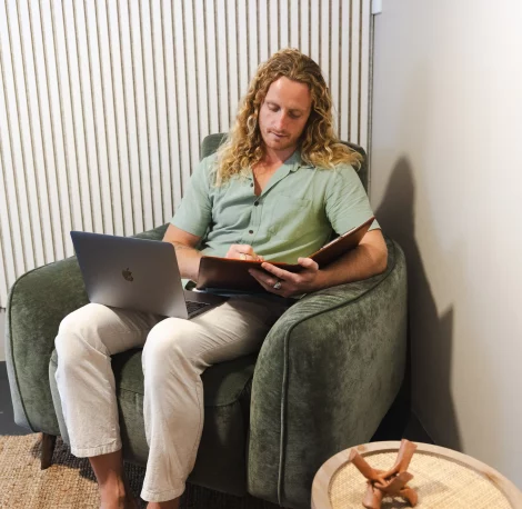 Male therapist Riley sitting on a brown leather couch at Nature Of Wellness in Currumbin, Gold Coast, providing online therapy.